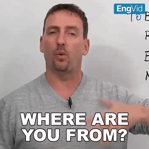 a man with a microphone on his neck says " where are you from " in front of a white board