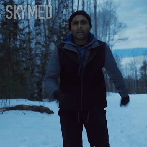 a man in a black vest is standing in the snow with the word skymed above him