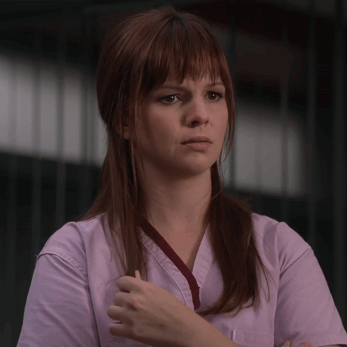 a woman with red hair is wearing a pink scrub top with a red ribbon around her neck