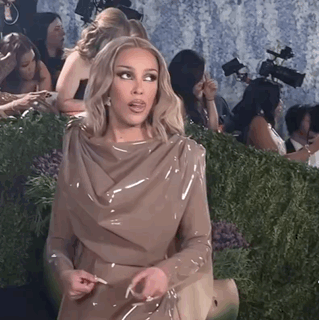 Doja Cat in a sculptural dress gives a questioning hand gesture at an event.
