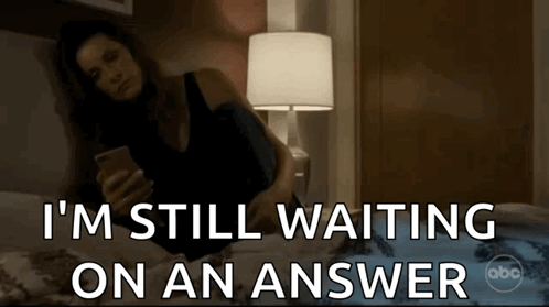 a woman laying on a bed looking at her phone with the words i 'm still waiting on an answer
