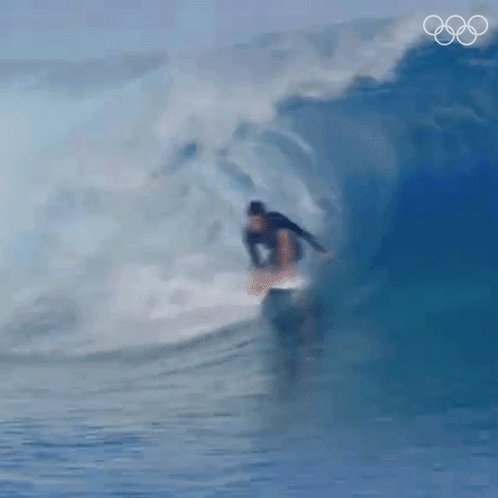 a surfer is riding a wave with the olympic rings behind him