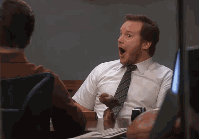 Andy Dwyer leans forward with his mouth agape at a table.