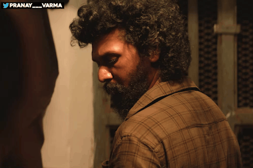 a man with curly hair and a beard is standing in front of a sign that says pranay