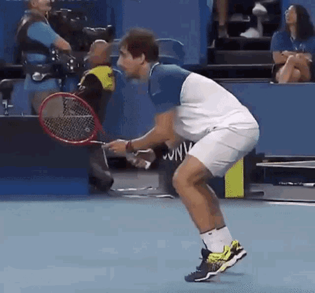 a man is holding a tennis racquet on a court while a woman sits in the stands