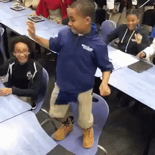 A schoolchild performs an enthusiastic dance move in a classroom.