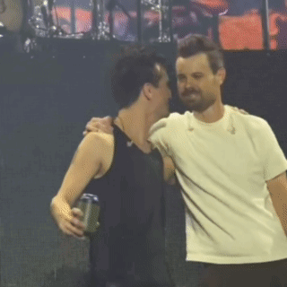 two men are hugging each other on a stage and one is holding a can of beer