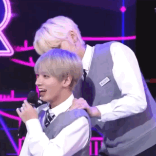 two men are standing next to each other on a stage and one of them is putting his hand on the other 's neck .