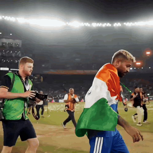 a man in a green vest is taking a picture of another man in a blue shirt