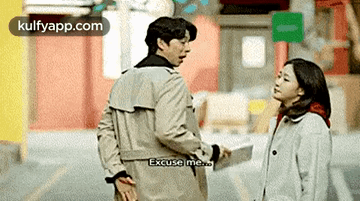 a man and a woman are standing next to each other on a street . the man is pointing at the woman .