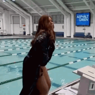 a woman is standing in front of a swimming pool with a sign that says asphalt green on it