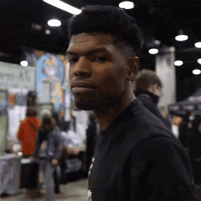 a man in a black shirt is looking at the camera with a crowd behind him