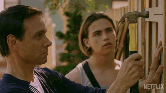 a man is hammering a nail into a wooden fence while another man watches