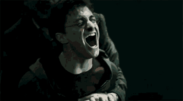 harry potter is holding a wand in his hand and screaming while being held by a man .
