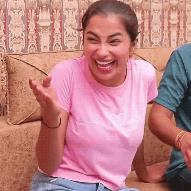 a woman in a pink shirt is laughing while sitting on a couch .