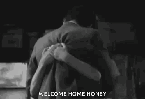 a black and white photo of a man and woman hugging each other with the words `` welcome home honey '' written on the bottom .