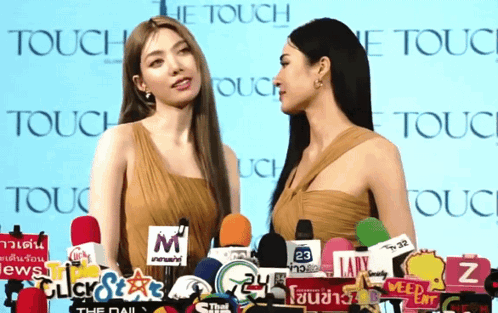 Two women at a TOUCH backdrop face one another while one gestures toward the other.