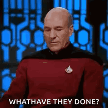 a bald man in a red shirt is sitting in front of a blue wall and asking what have they done .