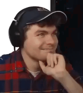 A man wearing headphones rests his hand against his face with a restrained smile.