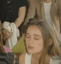 a woman with her eyes closed is sitting in a crowd of people with her mouth open .
