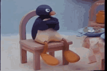 Pingu sits slumped at a tiny table looking bored and annoyed.
