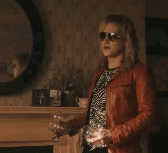 a woman wearing sunglasses and a leather jacket is holding a glass of wine .
