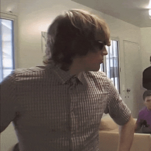 a man wearing sunglasses and a plaid shirt stands in a living room