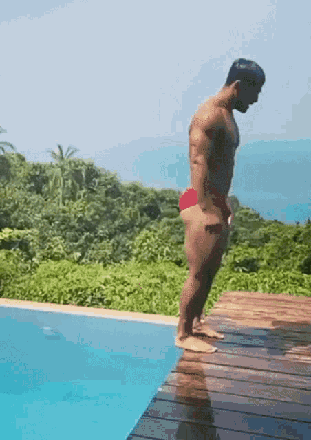 a man in a red swim suit is standing on a wooden deck next to a swimming pool .