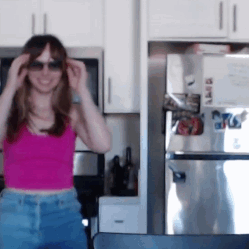 a woman wearing sunglasses and a pink tank top stands in front of a stainless steel refrigerator