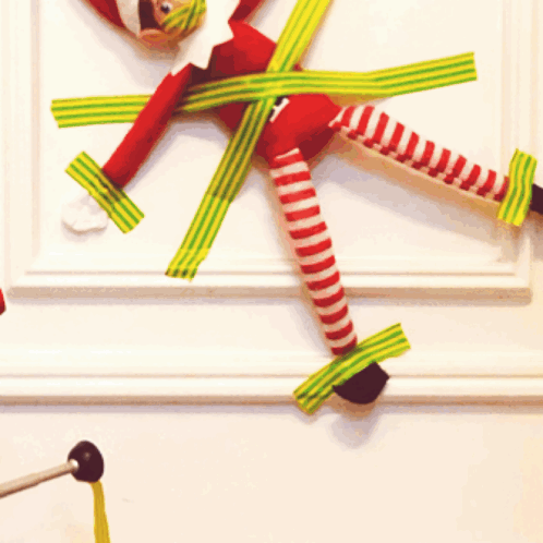 an elf on the shelf is taped to a white wall