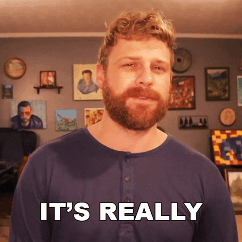 a man with a beard says it 's really in front of a wall of paintings