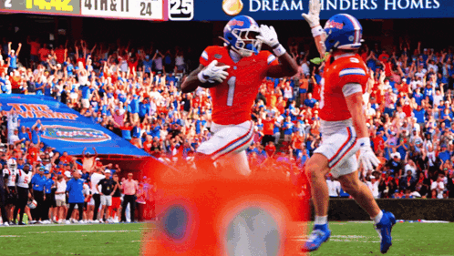 two football players celebrate a touchdown in front of a banner that says dream finders homes