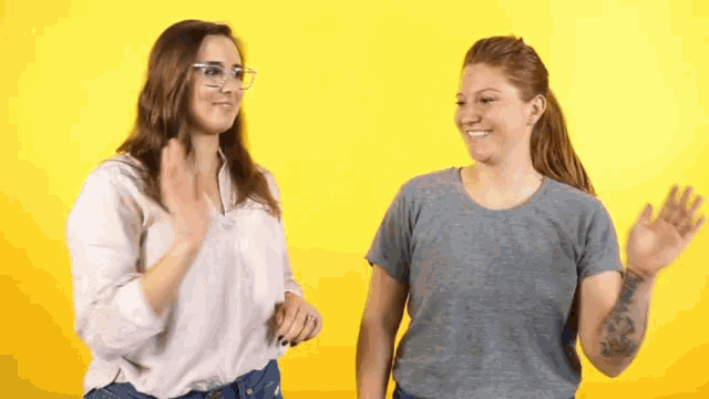Two women against a yellow background raise their hands for a high five.