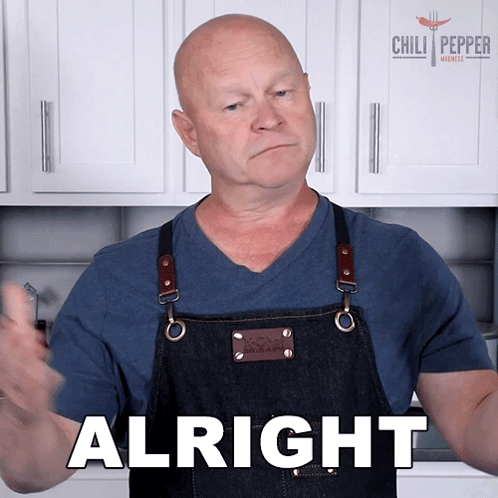 a man in an apron says alright in front of a chili pepper sign