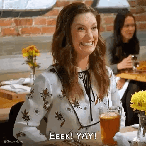 A smiling woman at a restaurant claps beside a drink as the caption reads “EEEK! YAY!”