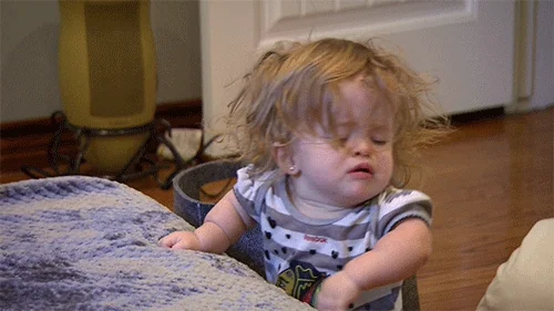 An exhausted toddler slumps forward and falls over on a bed.