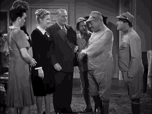 a black and white photo of a group of people standing around a man in a suit