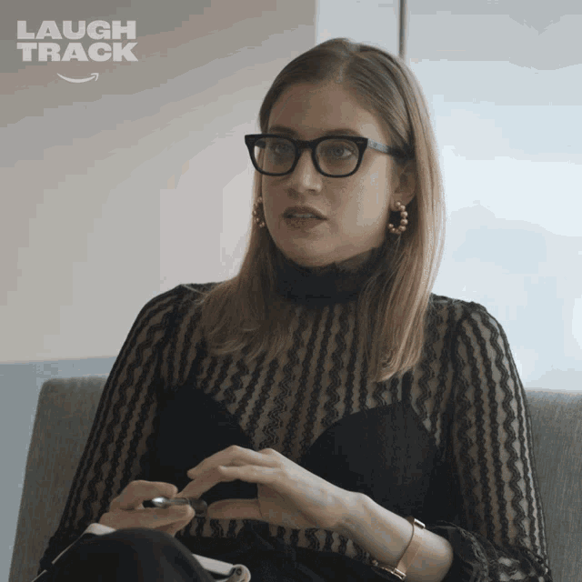 a woman wearing glasses is sitting in a chair with the words laugh track behind her