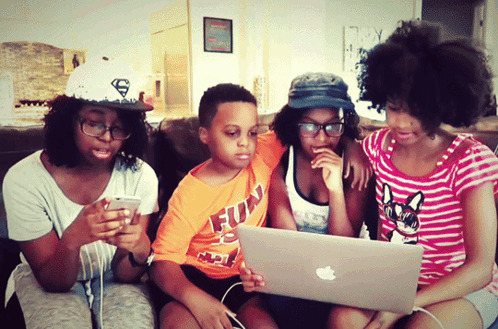 a boy wearing an orange shirt that says fun is looking at a laptop