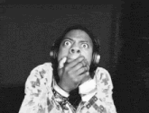 A person in headphones covers their mouth while trying not to react.