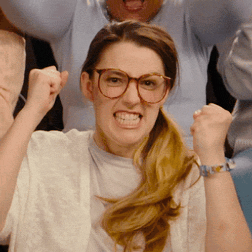A woman in glasses clenches both fists in an intense excited reaction.
