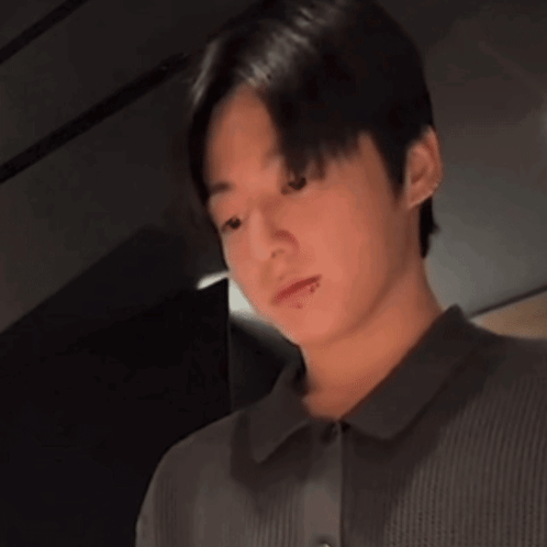 A man in a dark shirt looks down with a pouty, subdued expression.