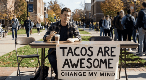 a man is sitting at a table with a sign that says tacos are awesome change my mind