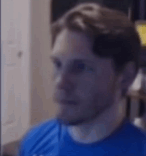 a man in a blue shirt is looking at the camera with a serious look on his face .