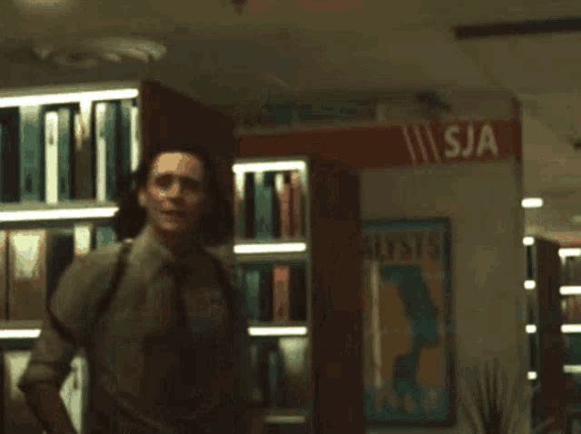 a man in a suit and tie is standing in front of a bookshelf .
