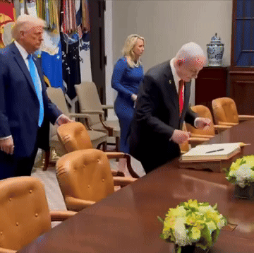 a man in a suit is signing a document while a woman stands behind him