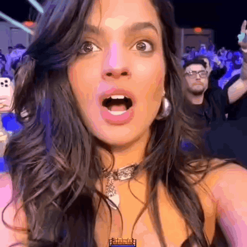 A woman at an event looks ahead with a dramatic wide-eyed gasp.