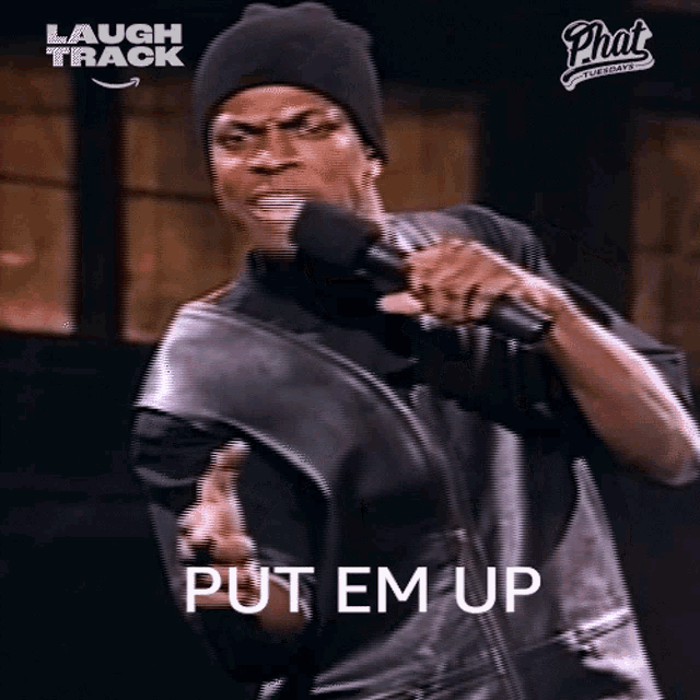 a man is holding a microphone and saying `` put em up '' while wearing a hat and a leather jacket .