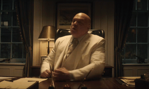 a man in a white suit sits at a desk
