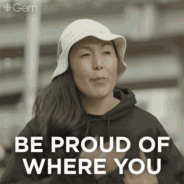 a woman wearing a white hat and a black hoodie says " be proud of where you "